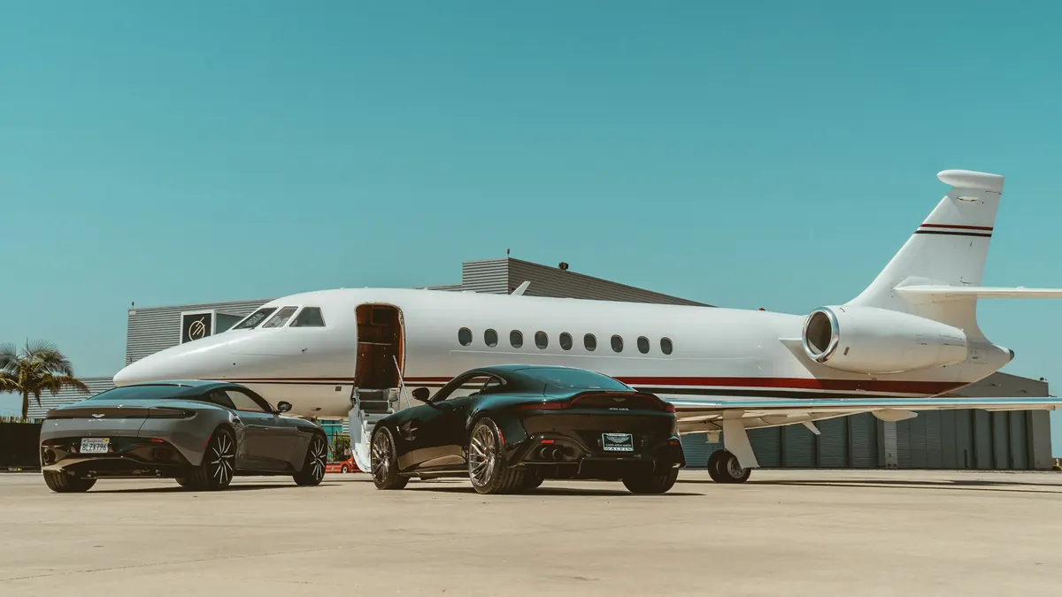 Two cars parked beside a business jet on a sunlit ramp